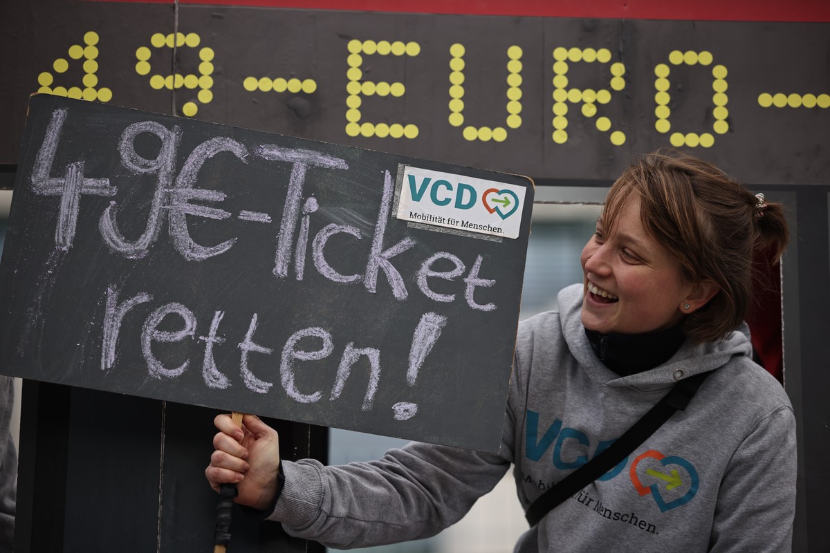 epa10960541 A protester holds a slate reading 'Save 49EUR-Ticket!!' as she looks out of a stylized bus window in front of the Chancellery during a staged protest for climate-friendly mobilit ...