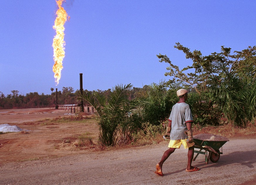 390464 36: A villager walks past a column of fire from the Oshie flare station owned by Italian oil company Agip, March 8, 2001 near Akaraolu, Nigeria. The natural gas flare was lit in 1972 and has be ...