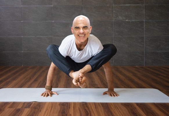 Alain Berset als Yogalehrer. Experienced yogi doing firefly pose variation in gym. Yogi concept. Front view.