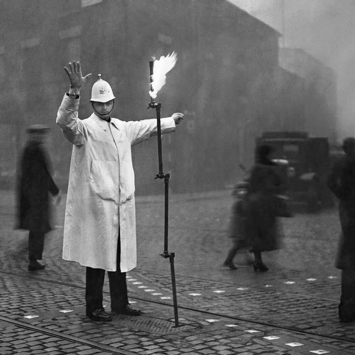 Ein Londoner Polizist, der den Verkehr im dichten Nebel regelt, benutzt ein Gerät, das an die Gasleitung angeschlossen ist und in einer Metallbox in der Straße versenkt werden konnte. (1935)