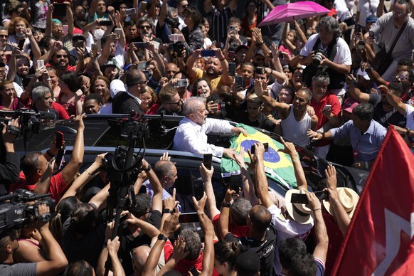 Former Brazilian President Luiz Inacio Lula da Silva, center, who is running for president again, holds a Brazilian flag surrounded by supporters after voting in a presidential run-off election in Sao ...