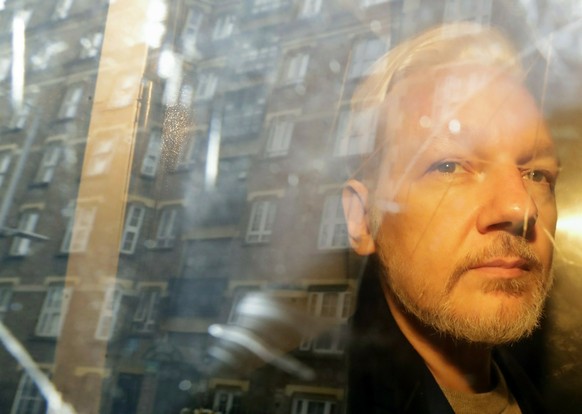 FILE - In this Wednesday May 1, 2019 file photo, buildings are reflected in the window as WikiLeaks founder Julian Assange is taken from court, where he appeared on charges of jumping British bail sev ...