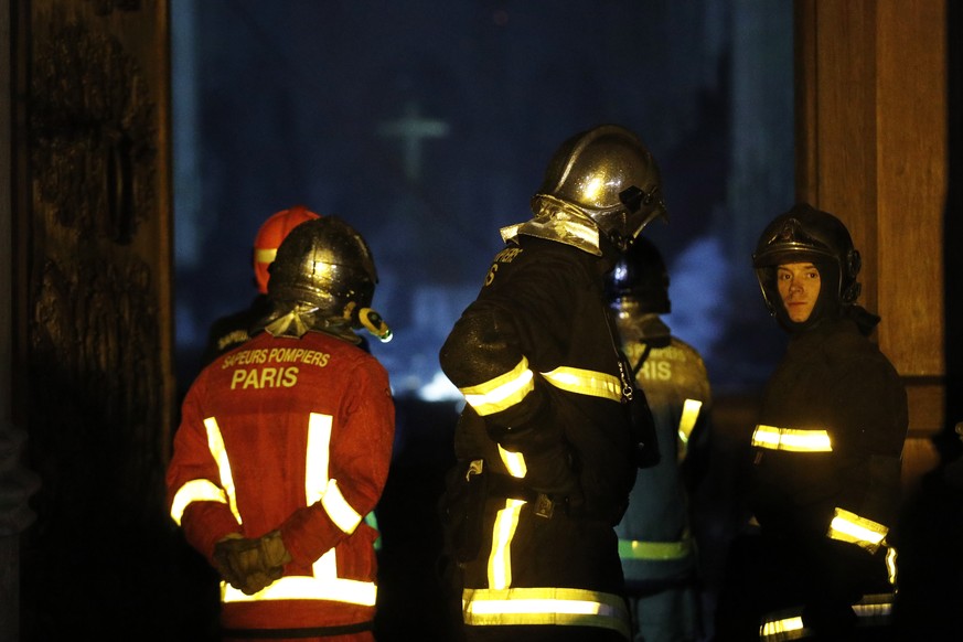 epa07509107 French firemen stand in front of a door while a fire is still burning the roof of the Notre-Dame Cathedral in Paris, France, 15 April 2019. A fire started in the late afternoon in one of t ...