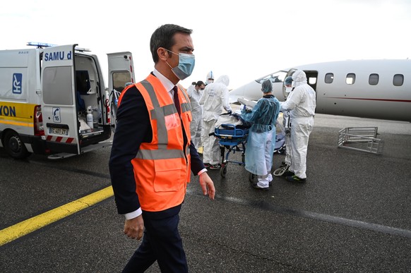 epa08823486 French Health Minister Olivier Veran watches as medical staff transport a patient on a stretcher to awaiting medical flight, to be evacuated to another hospital, at the Bron airport near L ...