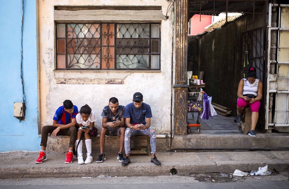People surf the internet on their smartphones on the sidewalk in Havana, Cuba, Thursday, Dec. 6, 2018. For the first time, Cubans are able to sign up for 3G internet service for their mobile phones, w ...