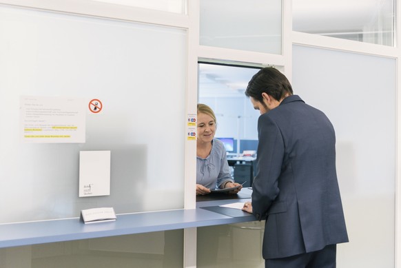 An employee of the Zug Commercial Registry receives a form from a customer at the counter, pictured in Zug, Switzerland, on March 1, 2018. The Commercial Registry is a public database that aims the pu ...