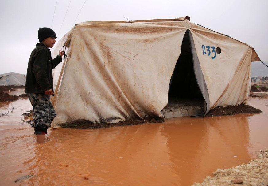 epa08071705 A Syrian boy walks through flood waters at Deyaa camp for internally displaced persons (IDPs), near the Turkish-Syrian border near Sarmada, northern Syria, 14 December 2019. According to l ...