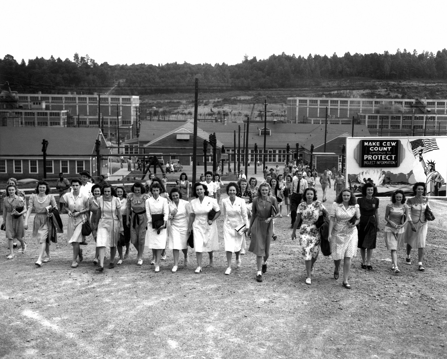 Shift change at the Y-12 uranium enrichment facility in Oak Ridge. 1944. Notice the billboard: &quot;Make CEW count Continue to protect project information.&quot; CEW stands for Clinton Engineer Works ...