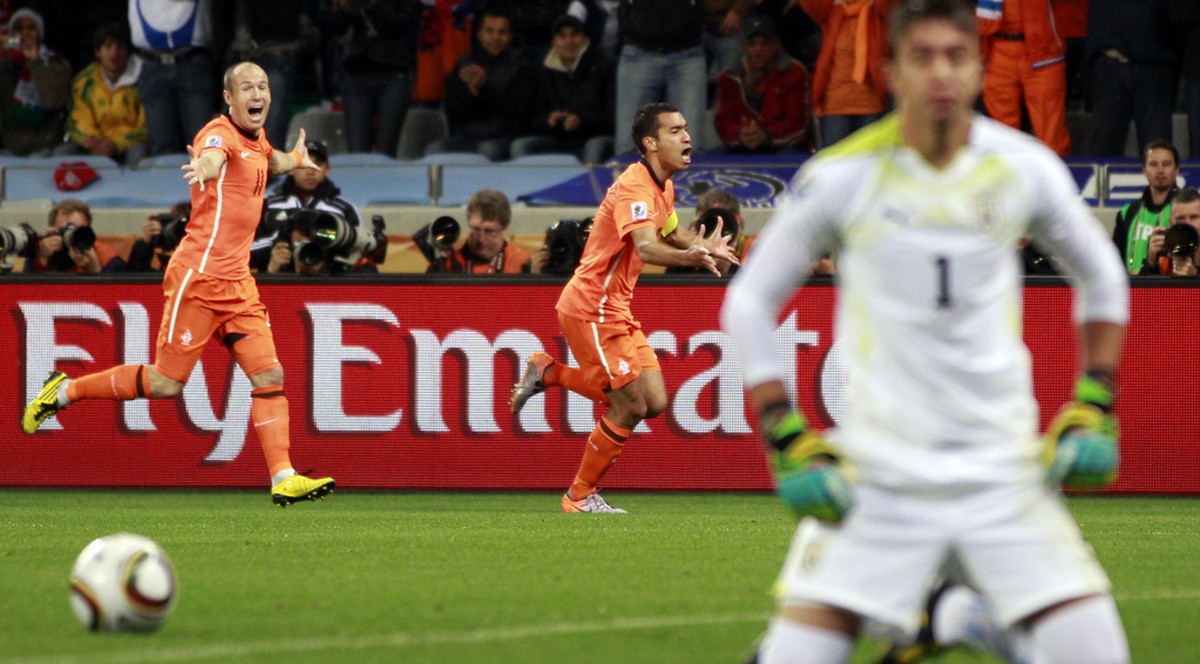 Netherlands' Giovanni van Bronckhorst, background center, celebrates with teammate Arjen Robben after scoring the opening goal as Uruguay goalkeeper Fernando Muslera, foreground right, reacts dur ...