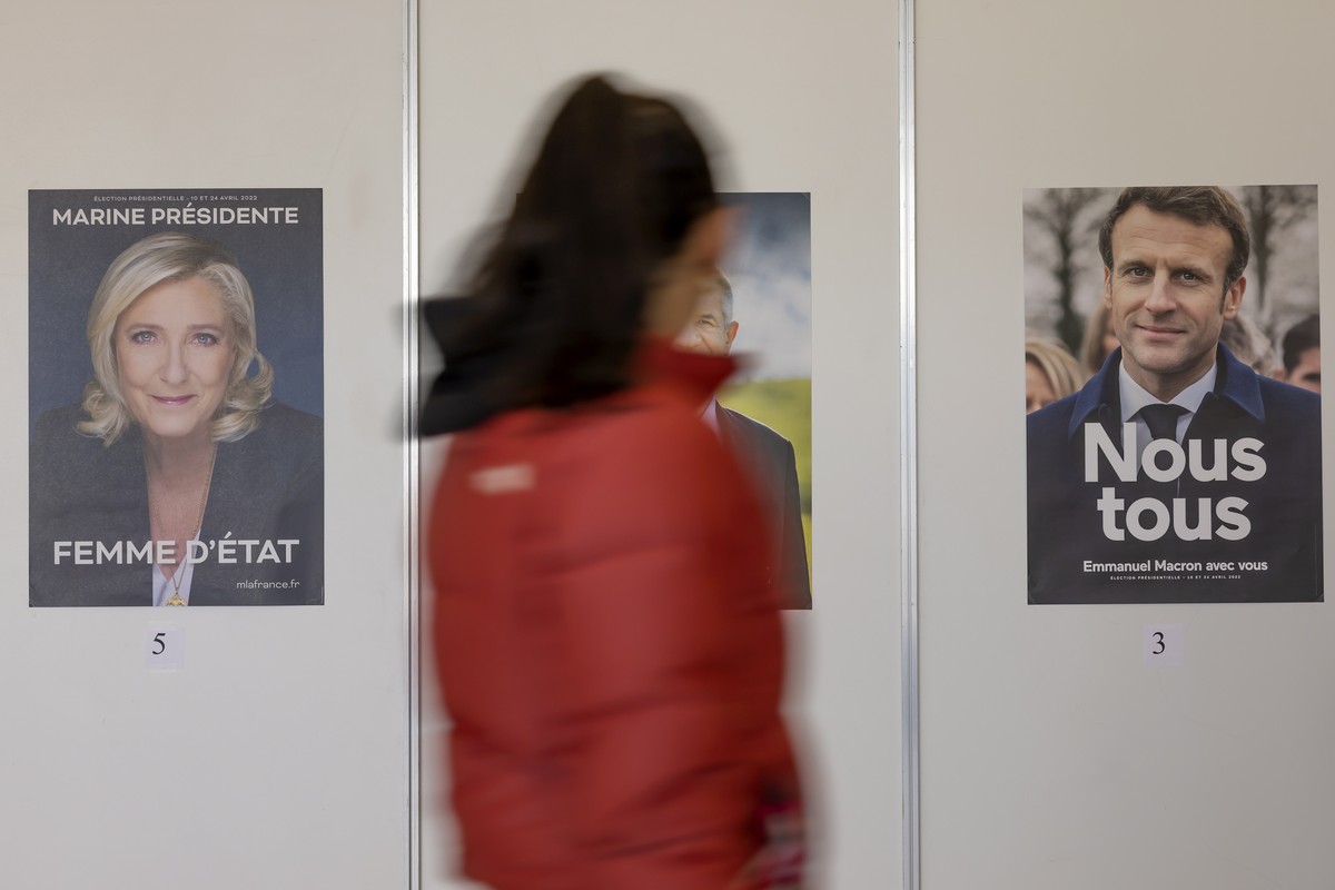 epa09882076 A voter walks past election posters of Marine Le Pen (L) and of Emmanuel Macron (R) for the French presidential election at the Palexpo polling station in Geneva, Switzerland, 10 April 202 ...