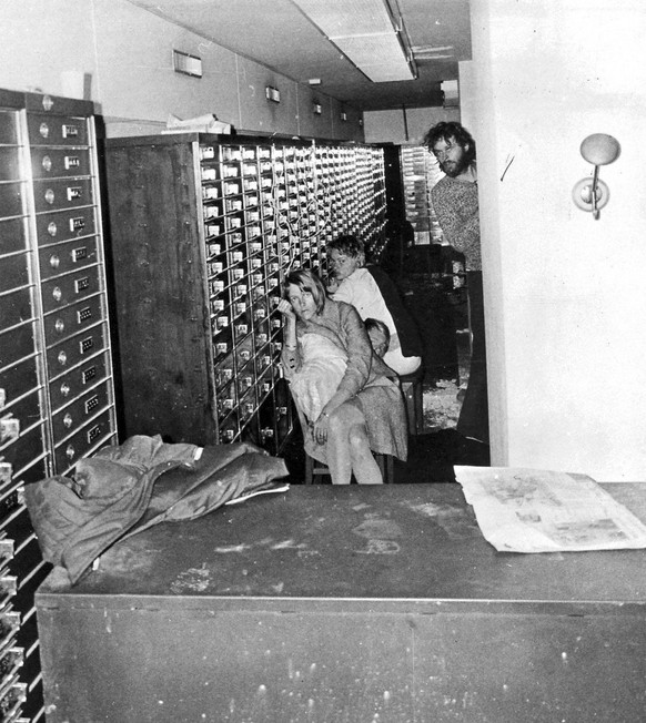 Bank robber Clark Olofsson, right, peers at the camera while two unidentified female hostages sit inside a bank vault in this Aug. 23,1973 photo. The photo was taken by a camera sent down by Swedish p ...