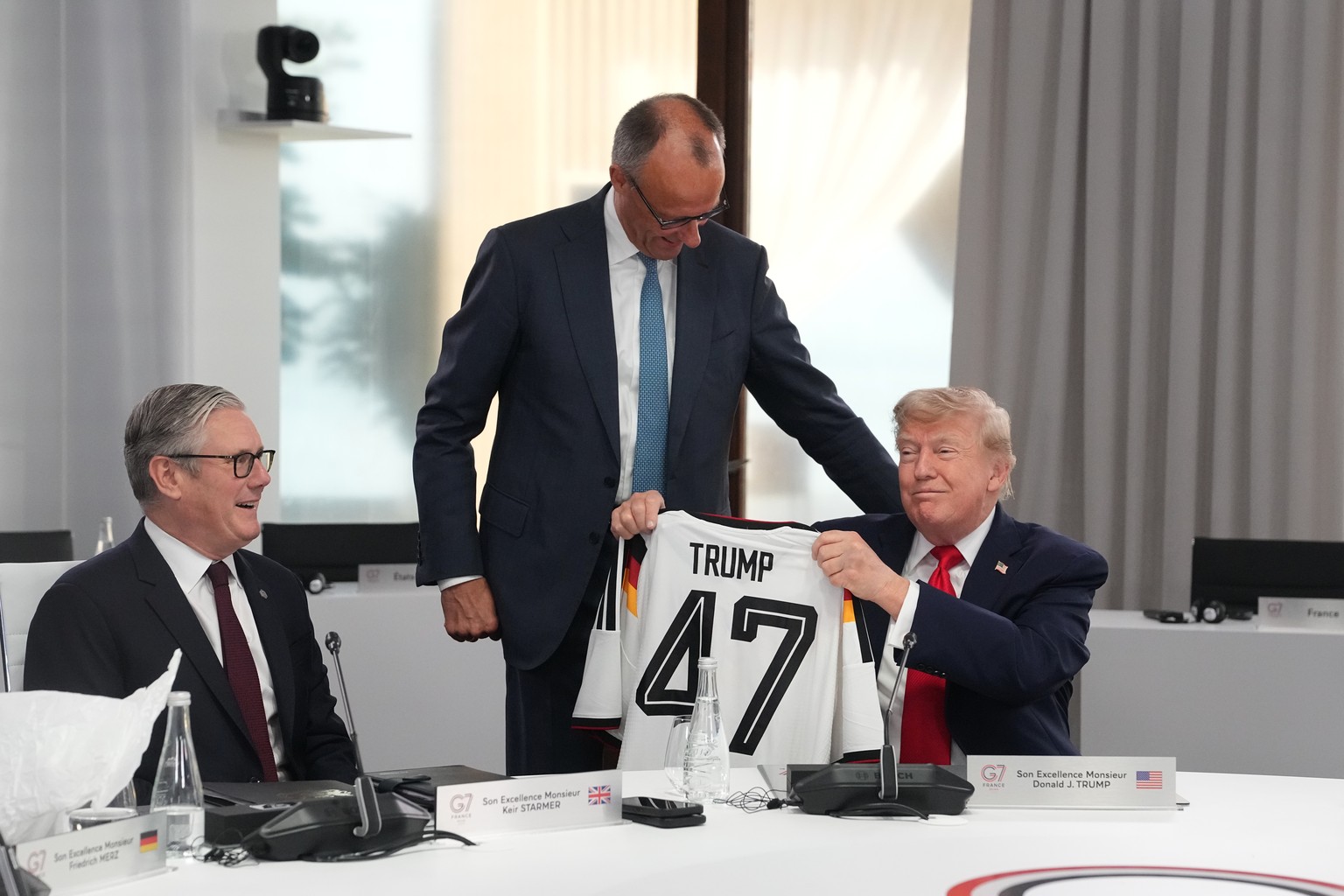 U.S. President Donald Trump, right, holds up a jersey with the number 47 on it as British Prime Minister Keir Starmer, left, and German Chancellor Friedrich Merz look on during a working session at th ...
