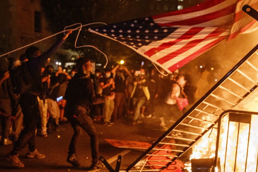 epa08457256 People throw a United States flag on a fire during a demonstration over the death of George Floyd, who died in police custody, near the White House in Washington, DC, USA, 31 May 2020. A b ...