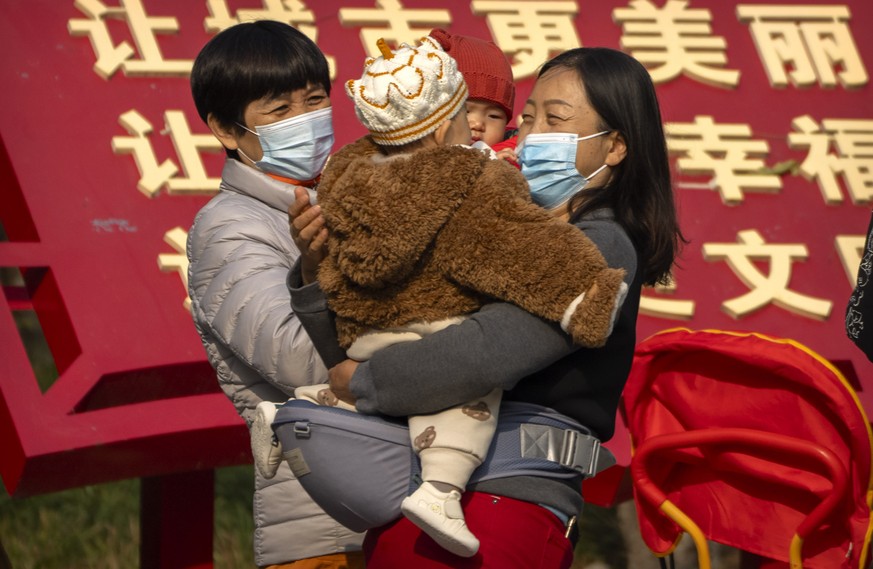 Women wearing face masks to protect against COVID-19 hold children as they stand at a public park in Beijing, Wednesday, Nov. 17, 2021. (AP Photo/Mark Schiefelbein)