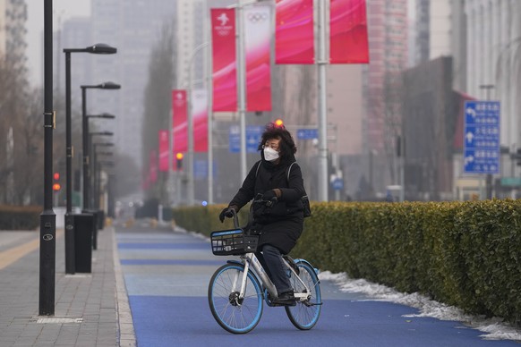 A woman wearing a face mask to help protect from the coronavirus cycles past the Beijing Winter Olympics banners on display along a street in Beijing, Sunday, Jan. 30, 2022. Beijing officials said Sun ...