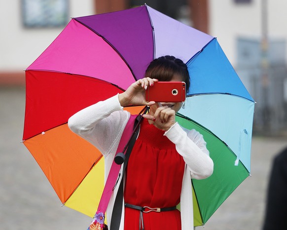 A Chinese tourist with a colorful umbrella takes a picture visiting the Roemerberg square in Frankfurt, Germany, on a warm Friday, July 29, 2016. (AP Photo/Michael Probst)