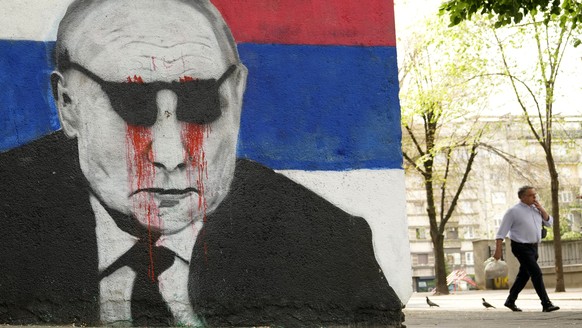 A man passes by a mural depicting the Russian President Vladimir Putin vandalized with paint, in Belgrade, Serbia, Saturday, May 7, 2022. Despite having to pay a big price Serbia for not introducing s ...