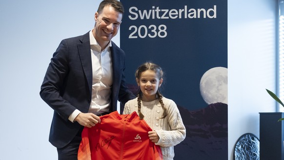 Dario Cologna, Vorstandsmitglied Switzerland 2038 und Vertreter der Athleten, uebergibt der jungen Langlauf-Athletin Malena Mueller eine Jacke, die er bei Olympia getragen hat, waehrend einer Medienko ...