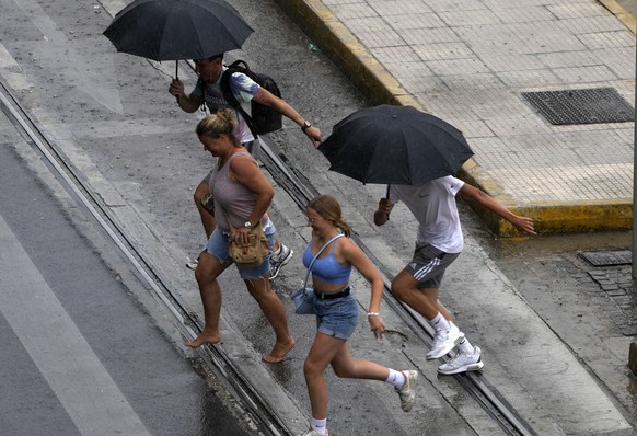 Tourists run as they try to avoid getting wet, during a heavy rainstorm in central Athens, Greece, Wednesday, Aug. 24, 2022. The last three days of storms has caused flooding on several thoroughfares  ...