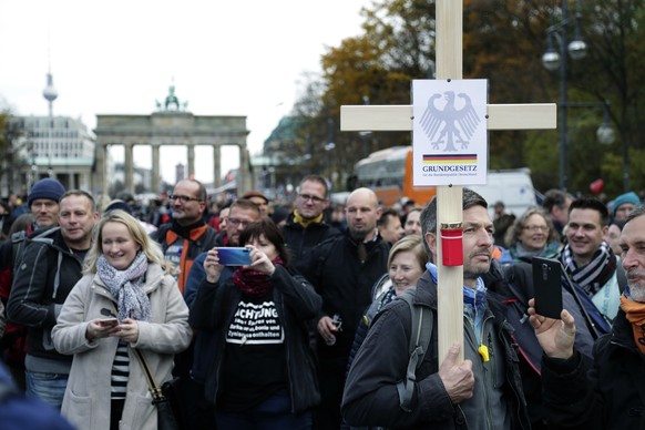 A man holds a cross with the inscription &#039;Constitution for the Federal Republic of Germany&#039; as he attends a protest rally in front of the Brandenburg Gate in Berlin, Germany, Wednesday, Nov. ...
