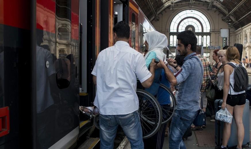 epa04906530 A migrants woman in a wheelchair is lifted on an Austrian train to Munich, Germany at the Keleti Railway Station in Budapest, Hungary, 31 August 2015. Migrants possessing valid documents a ...