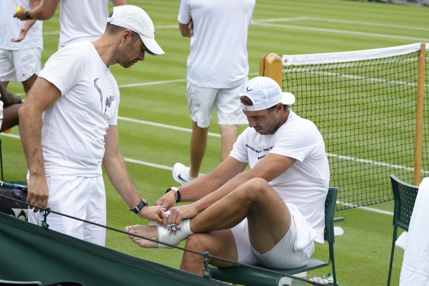 Rafael Nadal of Spain, right, adjusts bandages on his foot during a practice session ahead of the 2022 Wimbledon Championship at the All England Lawn Tennis and Croquet Club, Wimbledon, England in Lon ...