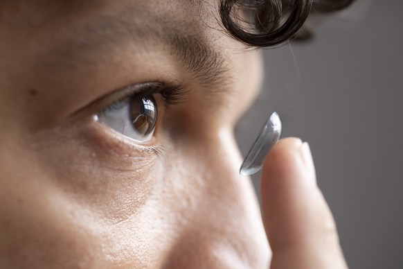 Extreme close up of a young male adult inserting a contact lens into his eye with his finger.