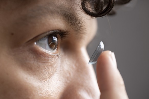 Extreme close-up of a young male adult inserting a contact lens into his eye with his finger.