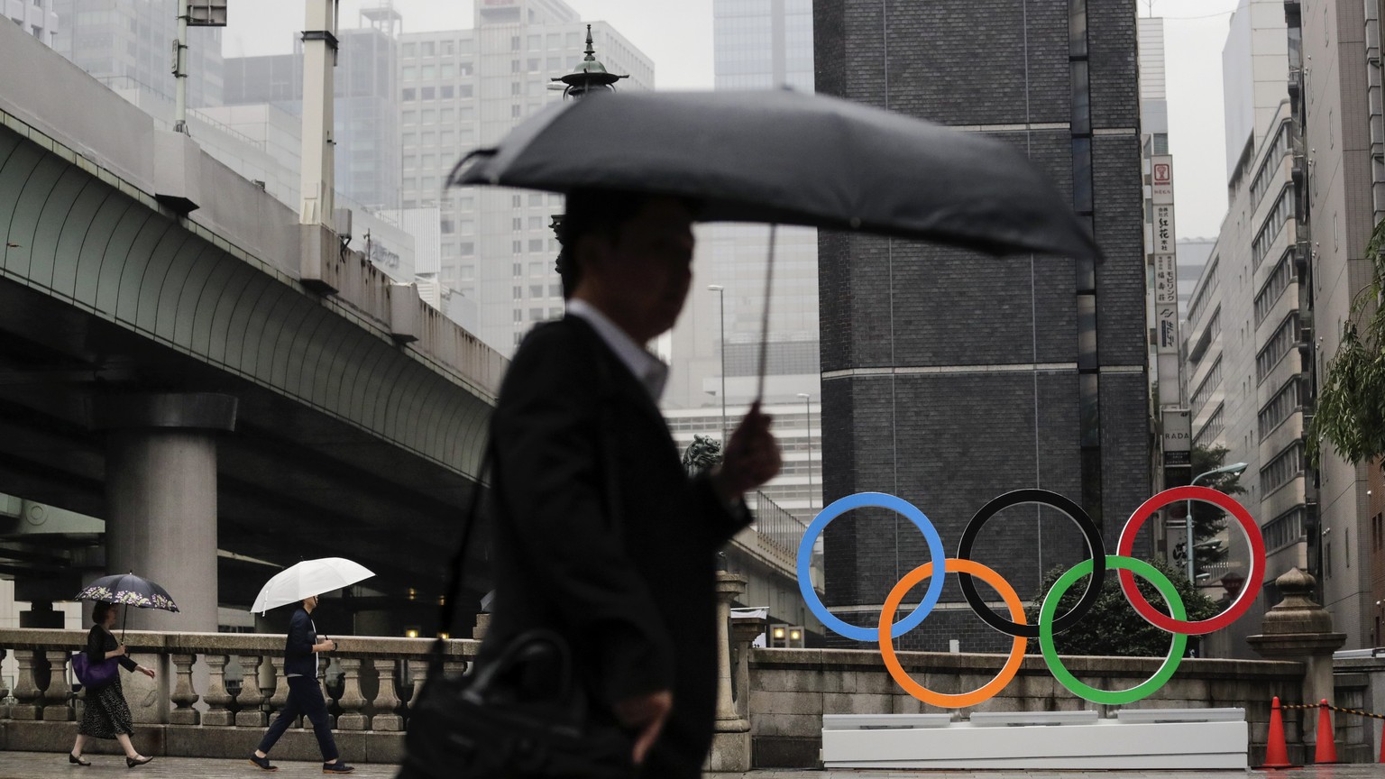 Commuters walk past the Olympic Rings Tuesday, July 23, 2019, in Tokyo. To mark the year-to-go mark, the gold, silver and bronze Olympic medals are to be unveiled Wednesday as part of daylong ceremoni ...