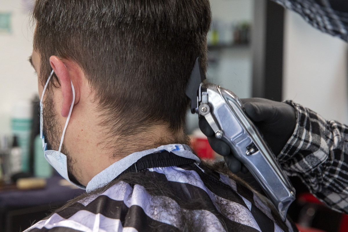 Kris, hairdresser, wearing a plastic protective mask with a protective face mask cuts the hair to a client which also wears protective face mask at the Saint's Barbershop, in Carouge near Geneva, ...