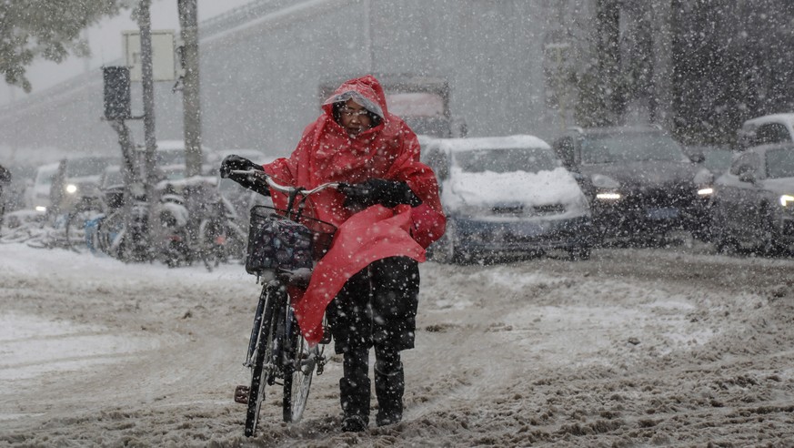 epa09569331 A woman pushes a bicycle in the street during a snowfall in Beijing, China, 07 November 2021. The Chinese National Meteorological Center on 06 November issued an orange alert for snowstorm ...