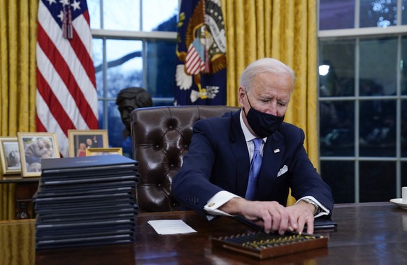 FILE - In this Jan. 20, 2021, file photo, President Joe Biden reaches for a pen to sign his first executive order in the Oval Office of the White House in Washington. Biden arrived at the White House  ...