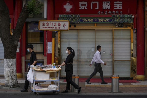 Workers wearing face masks push a trolley loaded with take away food past a closed hotpot restaurant on Monday, May 23, 2022, in Beijing. Beijing extended orders for workers and students to stay home  ...