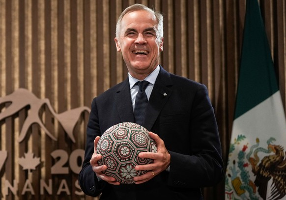 Canada&#039;s Prime Minister Mark Carney holds a soccer ball with beaded Huichol art on it after being gifted it by Mexican President Claudia Sheinbaum, not seen, before a meeting at the G7 Summit in  ...