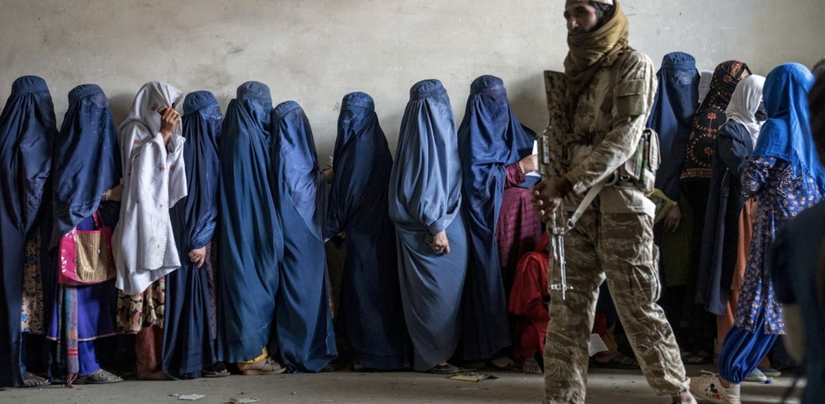 Un combattant taliban monte la garde pendant que des femmes attendent de recevoir des rations alimentaires distribuées par une organisation humanitaire, à Kaboul (Afghanistan), en mai 2023.