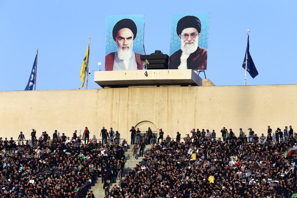 Iranian soccer fans sit under portraits of the late revolutionary founder Ayatollah Khomeini, left, and Supreme Leader Ayatollah Ali Khamenei, prior to start of the World Cup Group A qualifying soccer ...