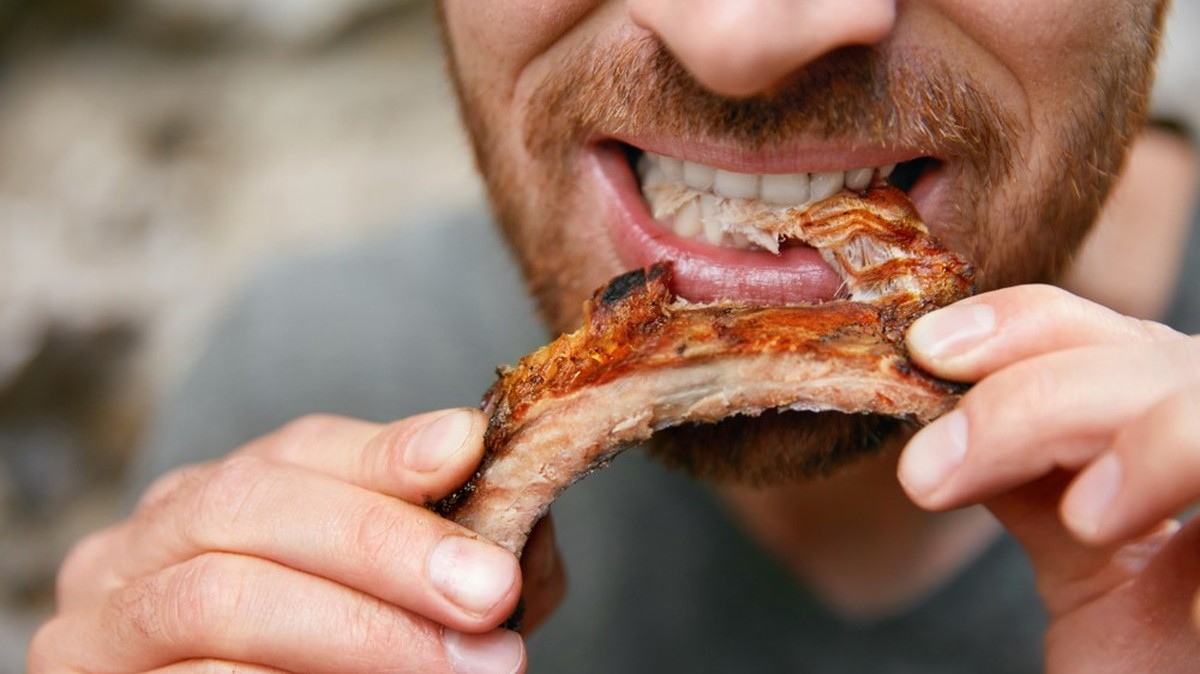 Ein Mann beisst in ein Stück Spareribs.
