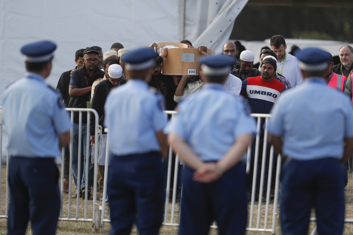 Police officials stand guard as mourners carry the body of a victim of the Friday, March 15 mosque shootings for a burial at the Memorial Park Cemetery in Christchurch, New Zealand, Friday, March 22,  ...