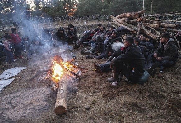 epa09579122 Asylum-seekers, refugees and migrants use fire to warm themselves in the camp at the Belarus-Polish border in the Grodno region, not far from the checkpoint Bruzgi, Belarus, 12 November 20 ...