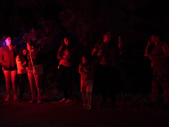 Onlookers are illuminated by police lights at the scene where officials say dozens of people have been found dead and multiple others were taken to hospitals with heat-related illnesses after a semitr ...