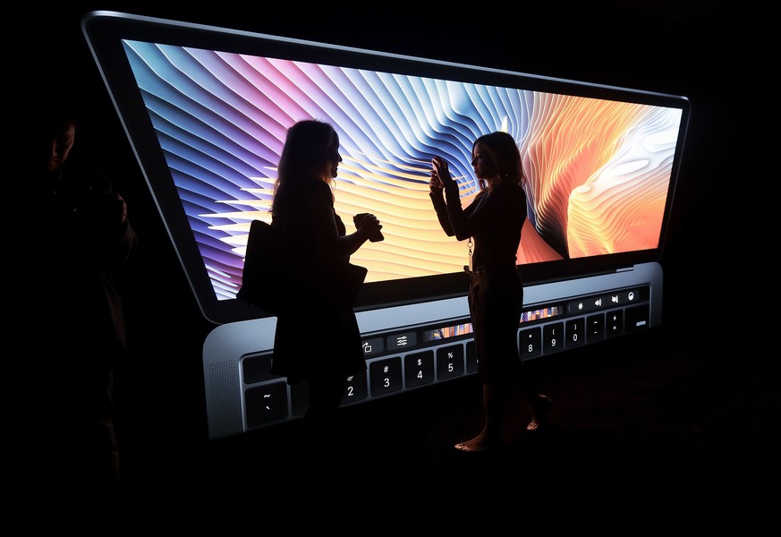 Women take photos in front of a large photo displayed of a MacBook computer in a demo room following the announcement of new products at Apple headquarters Thursday, Oct. 27, 2016, in Cupertino, Calif ...