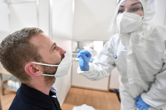An employee in protective clothing takes a swab from a man in the Corona test centre at the trade fair in Erfurt, Germany, Wednesday, April 28, 2021. The rapid test centre is operated primarily for vi ...