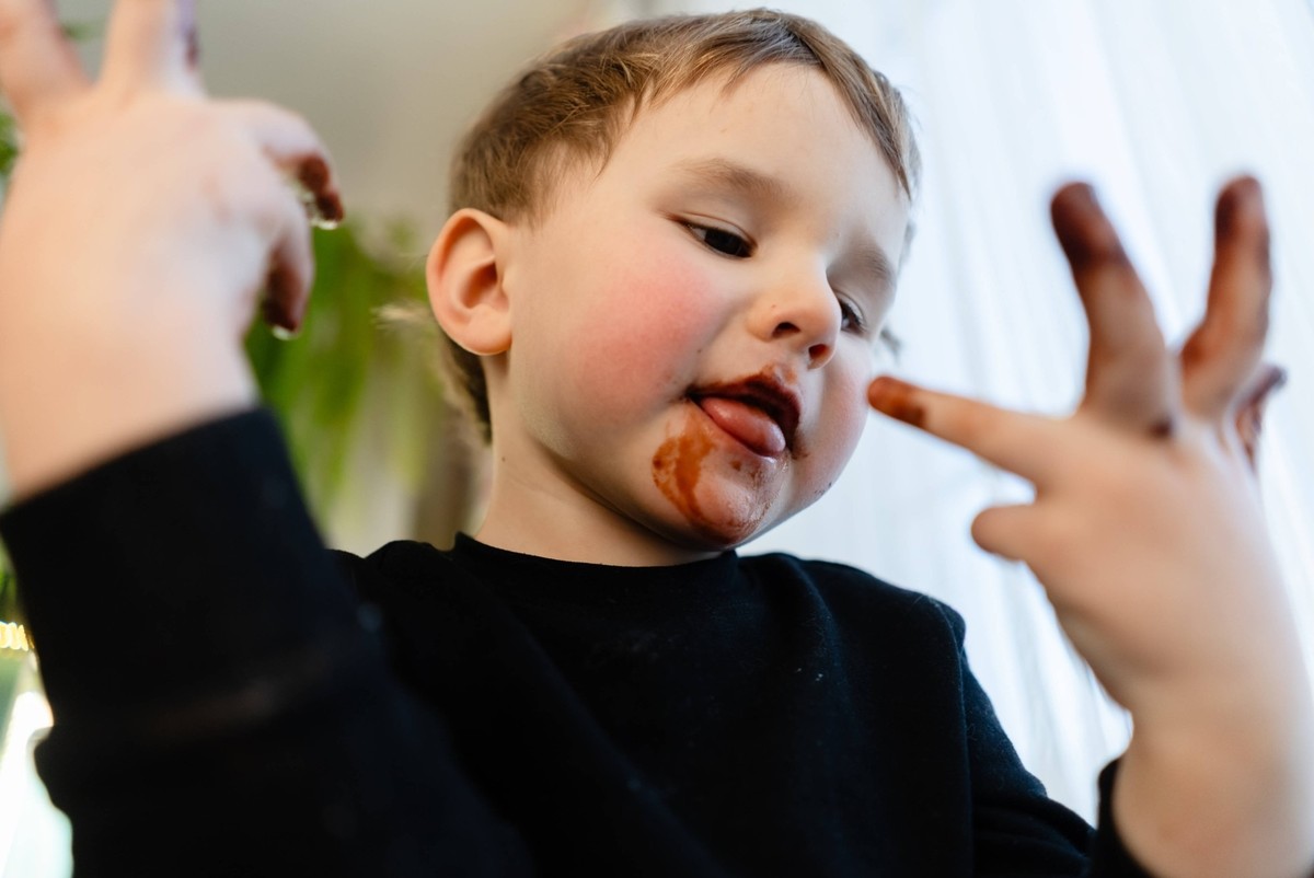 Ein Kind, das gerade dabei ist, sich die klebrigen Schokoladenh�nde abzulecken A three year old child about to lick sticky melted chocolate from fingers. Focus on hands and mouth. Concept of forbidden ...