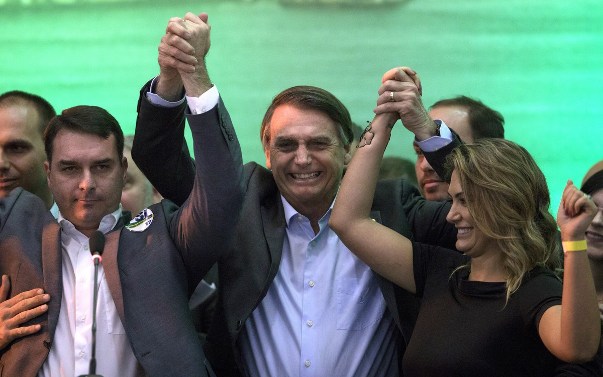 FILE - In this July 22, 2018 file photo, Brazil's presidential candidate Jair Bolsonaro, center, holds hands with his wife Michelle and son Flavio before supporters during the National Social Lib ...