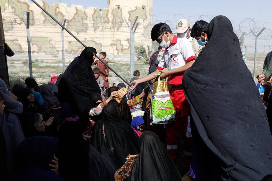 epa09420828 A handout photo made available by Iranian Red Crescent shows a member of Iranian Red Crescent distributes foods among Afghan Afghan refugee gather in Iran-Afghanistan border in Sistan-Bloc ...