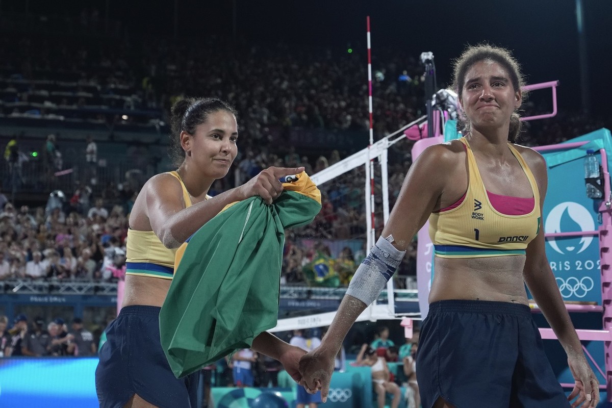 Brazil's Ana Patricia Silva Ramos, right, and Eduarda "Duda" Santos Lisboa hold hands after winning their women's beach volleyball gold medal match against Canada, at the 2024 Summ ...