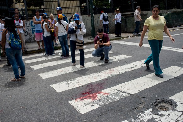 epa05915793 Passersby photograph the bloostain of a 17-year old boy who was shot and killed during an opposition protest in Caracas, Venezuela, 19 april 2017. Police, using tear gas, dispersed protest ...