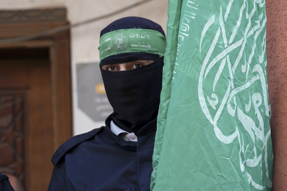 Masked militant from the Izzedine al-Qassam Brigades, the military wing of Hamas, waves the green flag of the Islamist group during a protest in support of Palestinian prisoners in Israeli jails, afte ...