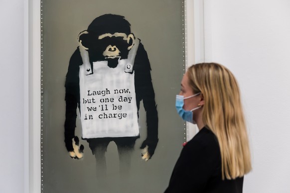 epa09293087 A gallery assistant poses with the work 'Laugh Now' by anonymous British street artist Banksy during a photocall of major summer auctions at Sotheby's Auction House in Londo ...