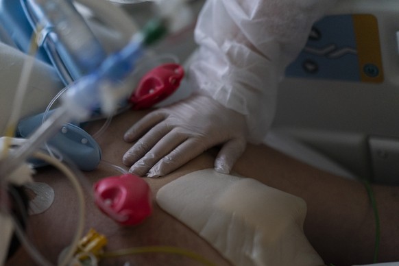 Katy Zalinian places her hand on her cousin who is suffering with COVID-19 and on a ventilator in the intensive care unit at the la Timone hospital in Marseille, southern France, Thursday, Dec. 23, 20 ...